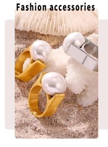 Detailed view of oversized white pearls on geometric gold and silver rings over coral