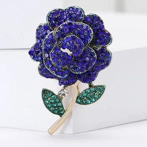 Close-up of rose brooch with deep blue rhinestones and green leaves on gold stem