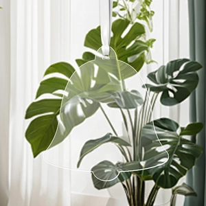 Clear acrylic bell ornament with white ribbon hanging against a botanical background