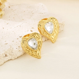 Dettaglio orecchini a cuore dorati con zircone a goccia e trama martellata su pietra