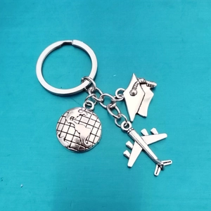 Silver travel keychain with compass, airplane, and graduation cap on blue background