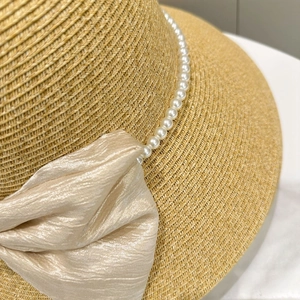 Close-up of the champagne satin bow and white pearl strand on a woven straw sun hat