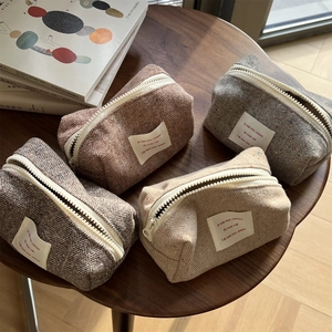 Herringbone tweed cosmetic bags in four colors arranged on a wooden table with books