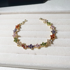 Golden clover bracelet with colorful teardrop gemstones on a jewelry display tray
