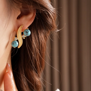 Detail of vintage gold feather earrings with turquoise beads and crystals on a model