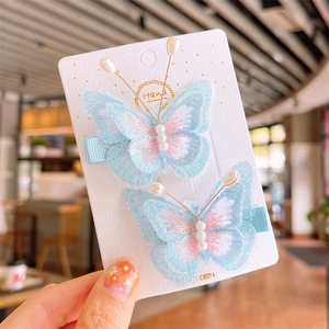Detailed embroidery on light blue and pink butterfly hair clips with pearl accents