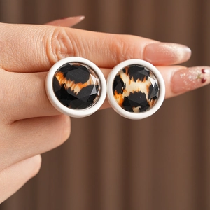 Close-up of a faceted leopard print round stud earring held between fingers