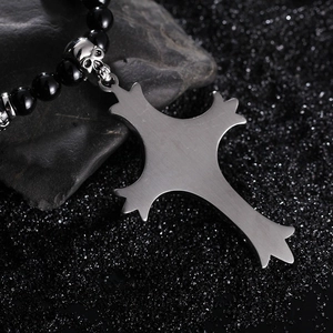 Gothic men's stainless steel skull cross pendant on black beaded chain over dark sand