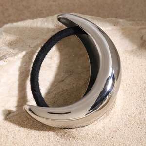 Close-up of silver crescent metal hair tie on natural stones and sand outdoor setting