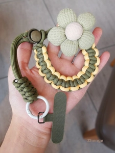 Close-up of army green braided phone lanyard with a fabric flower charm and metal ring