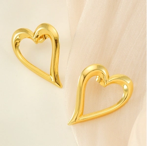 Macro shot of gold-plated hollow heart earrings on soft silk fabric background