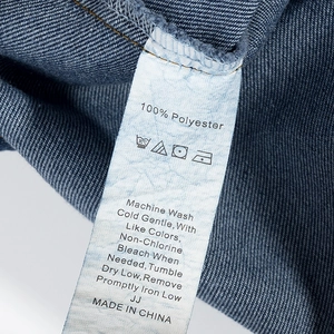 Makrodetail des Pflegeetiketts für das Jeanskleid mit 100% Polyester und Waschanleitungen