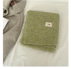 Detail of wool-blend egg label on green and yellow knitted scarf next to beige coat