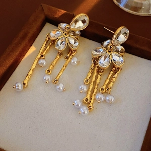 Macro shot of gold floral earrings with crystal pavé, chain tassels and white pearls
