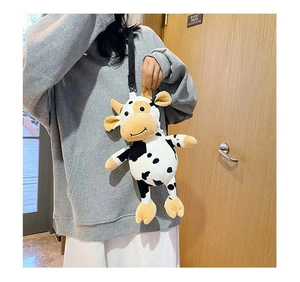 Detail showing plush cow crossbody bag with black spots worn by model over grey hoodie
