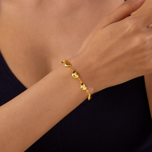 Detailed view of a gold-tone heart link chain bracelet worn on a female wrist