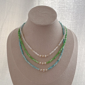 Close-up of stacked bamboo-style beaded necklaces with natural pearls in three vibrant colors