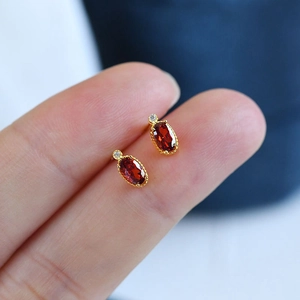 Close-up of vintage oval red gemstone stud earrings held by hand for size reference