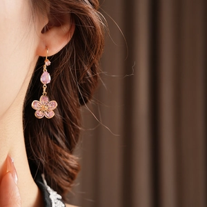 Close-up of golden flower drop earrings with pink zircon stones worn by a model
