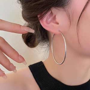 Close-up of a model wearing minimalist silver-toned large smooth hoop earrings in style