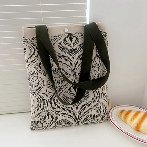 Close-up of beige knit tote bag with dark green floral pattern and snap closure detail