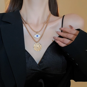 Detailed close-up of double-layer vintage gold evil eye and hammered disk necklaces