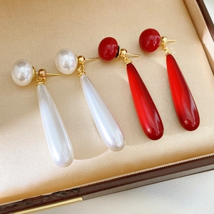 Detail view of drop-shaped resin pearl earrings in white and red inside a jewelry box
