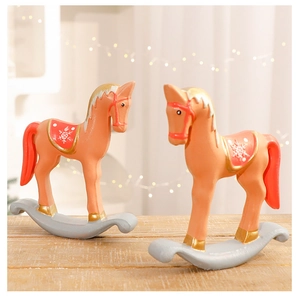 Close-up of two warm pink rocking horse Christmas ornaments on a rustic wood surface