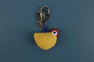 Close-up of yellow handmade crochet chick keychain with red comb and golden metal clasp