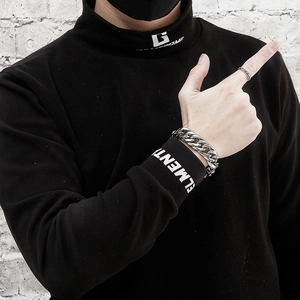 Detail eines silbernen Stahl-Panzerarmbands und Rings auf einem schwarzen Rollkragen