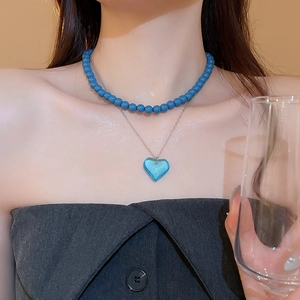 Detail of a double-layered necklace featuring blue beads and a heart-shaped pendant