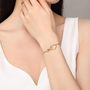 Detailed view of a gold double heart bracelet with zircon stones on a woman wrist