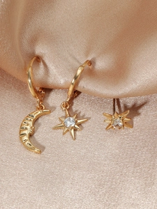 Macro shot of gold moon and star earring set with zircon on champagne silk fabric