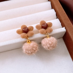 Detailed close-up of brown flocked flower earrings with soft cream pom-pom pendants