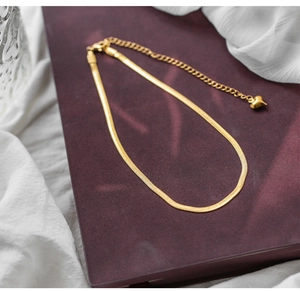Detail of gold snake chain necklace with adjustable heart pendant on red surface
