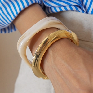 Detail of stacked chunky golden metal and marble resin bangles on a model wrist