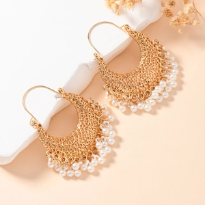 Détail de boucles d'oreilles bohèmes dorées avec motifs ajourés et pompons de perles