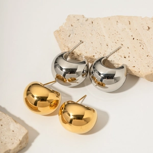 Minimalist 18k gold and silver thick C-shape hoop earrings on beige stone display