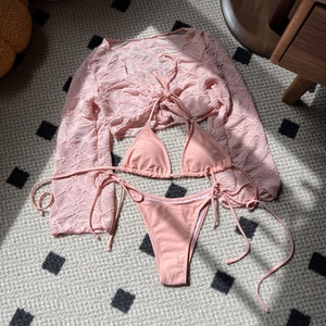 Detailed view of pink three-piece swimsuit with textured mesh cover-up and bikini set