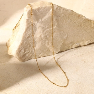 Collana a catena con perline dorate esposta su una roccia bianca in stile chic