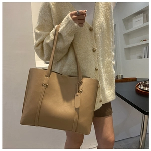 Detail of a large khaki leather tote bag with fine stitching on a model for daily commute