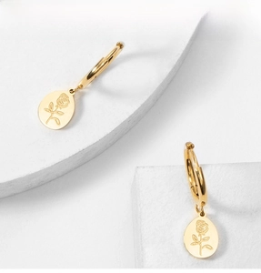 Close-up of golden hoop earrings featuring a textured oval rose pendant on a stone surface