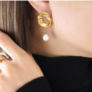 Close-up of irregular hollow gold-plated earrings with white drop freshwater pearl pendant