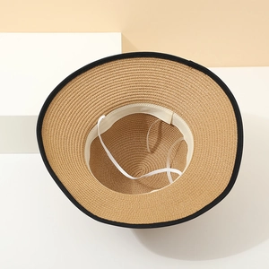 Detail view of woven straw sun hat interior with white elastic chin strap and black trim