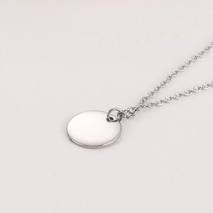 Vue macro d'un pendentif disque rond poli en acier inoxydable sur une fine chaîne argent