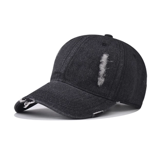 Detail of distressed ripped edges on a washed black denim baseball cap with vintage finish