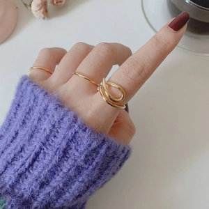 Close-up of a minimalist golden curved knot ring on model wearing purple knitwear