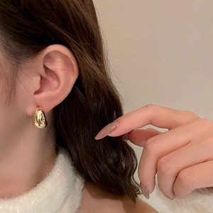 Close-up of golden teardrop stud earring on model with polished metallic finish