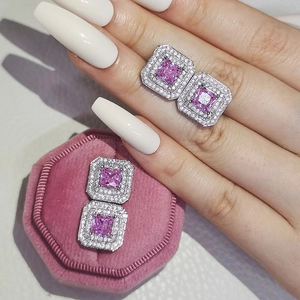 Detail view of pink square stud earrings with double halo zirconia stones on a hand