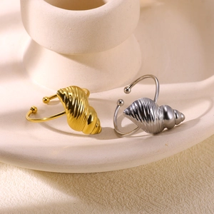 Detailed view of gold and silver conch-shaped open rings on a minimalist ceramic base